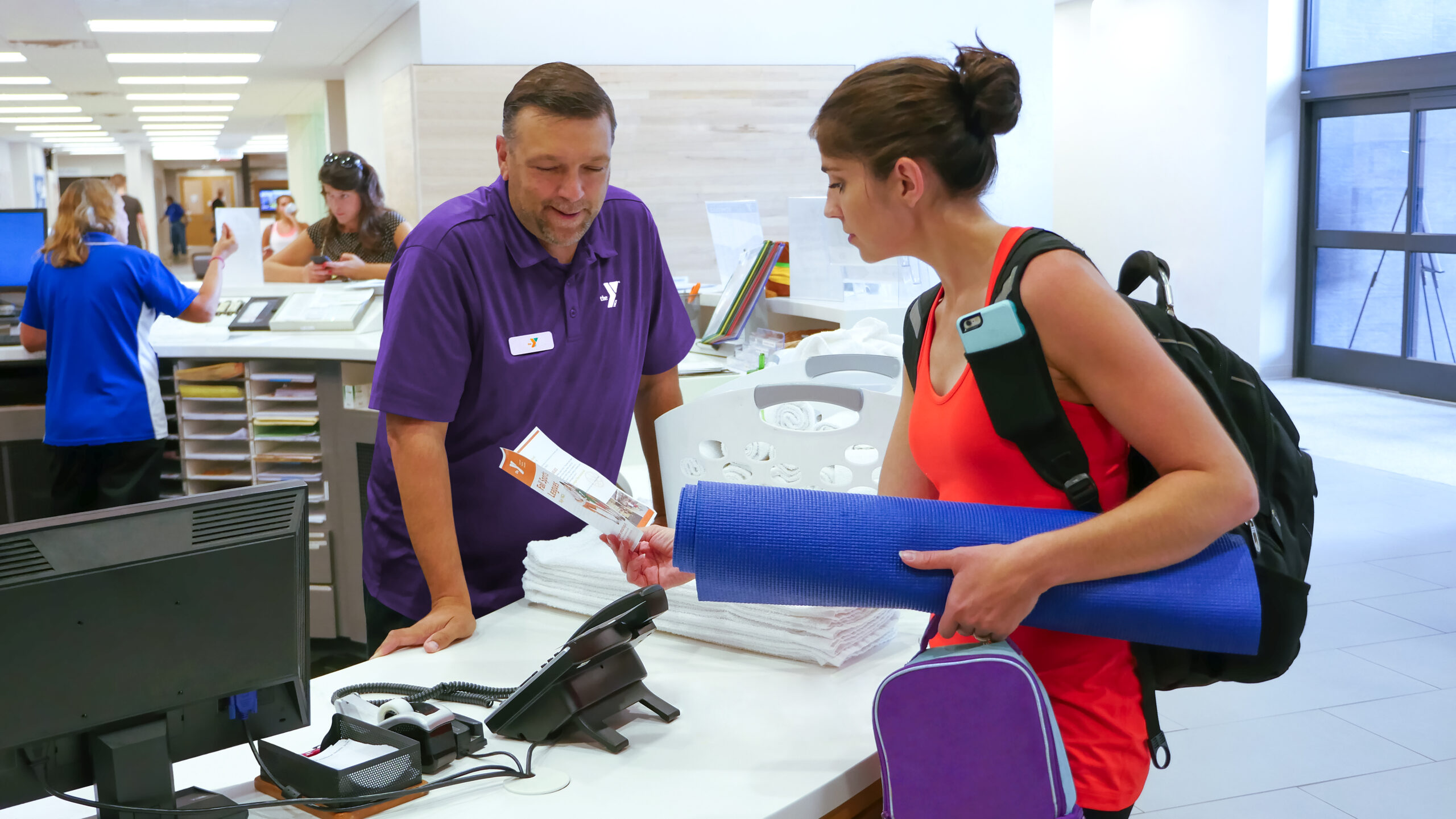 YMCA team member standing at the welcome desk wearing a purple golf shirt