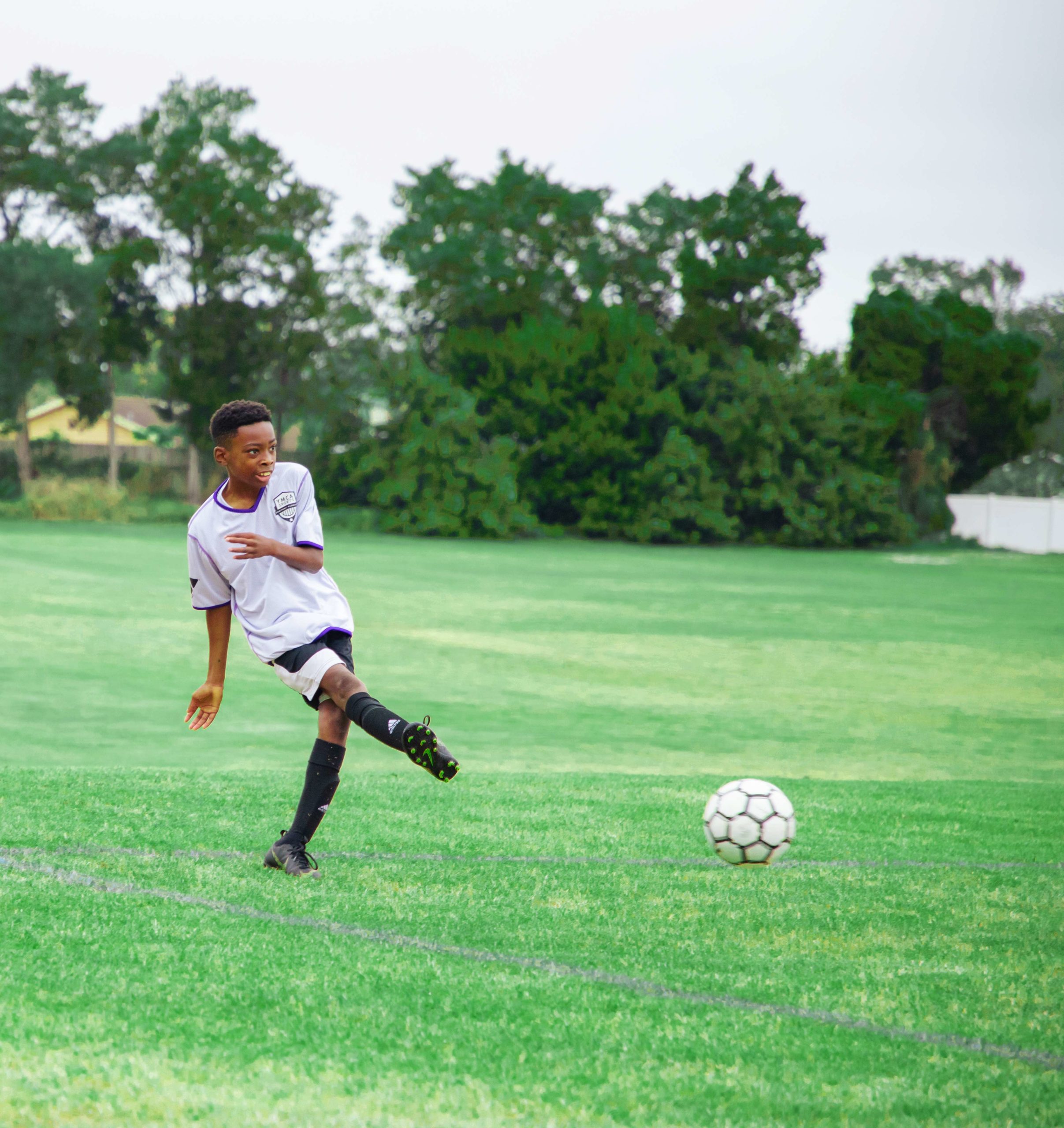 Boy kicking soccer ball on soccer field wearing YMCA uniform
