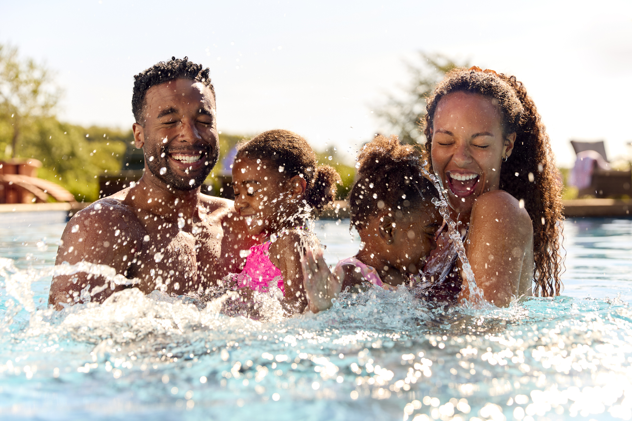 Family On Summer Holiday With Two Girls Being Held In Swimming Pool By Parents And Splashing