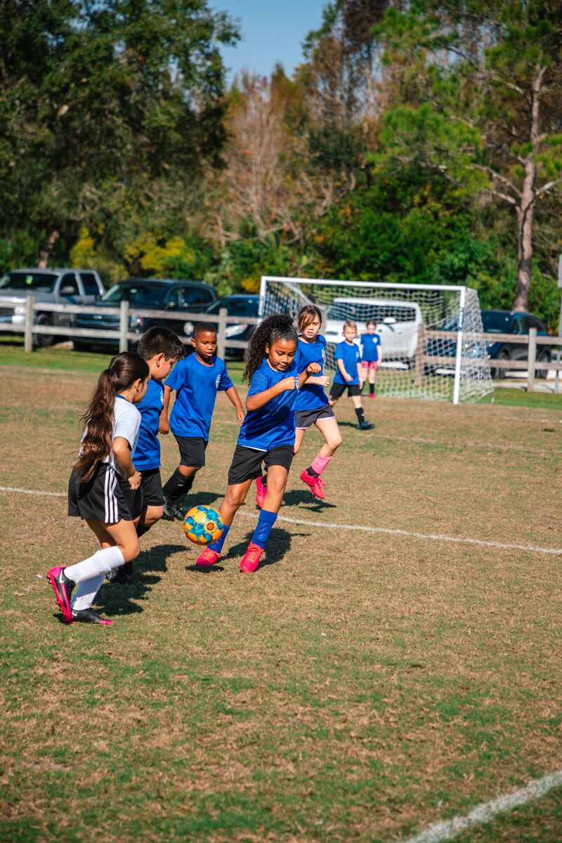 Group of kids chasing soccer ball on a soccer field during a soccer game while wearing YMCA uniforms